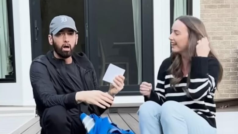 A man and a woman sit on a deck, the man holds  a photo and looks shocked