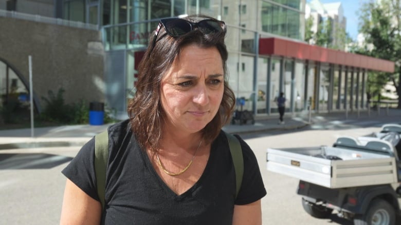 A dark-haired woman with black sunglasses on her head leans forward, with a street visible in the background.