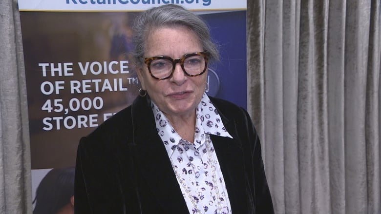 A woman with long-grey hair in a bun. She wears a patterned collared shirt and blazer.