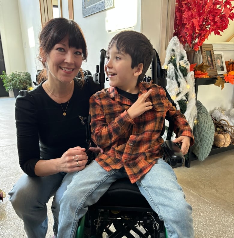 A smiling mother poses with a photo with her young son, who is in a wheelchair.