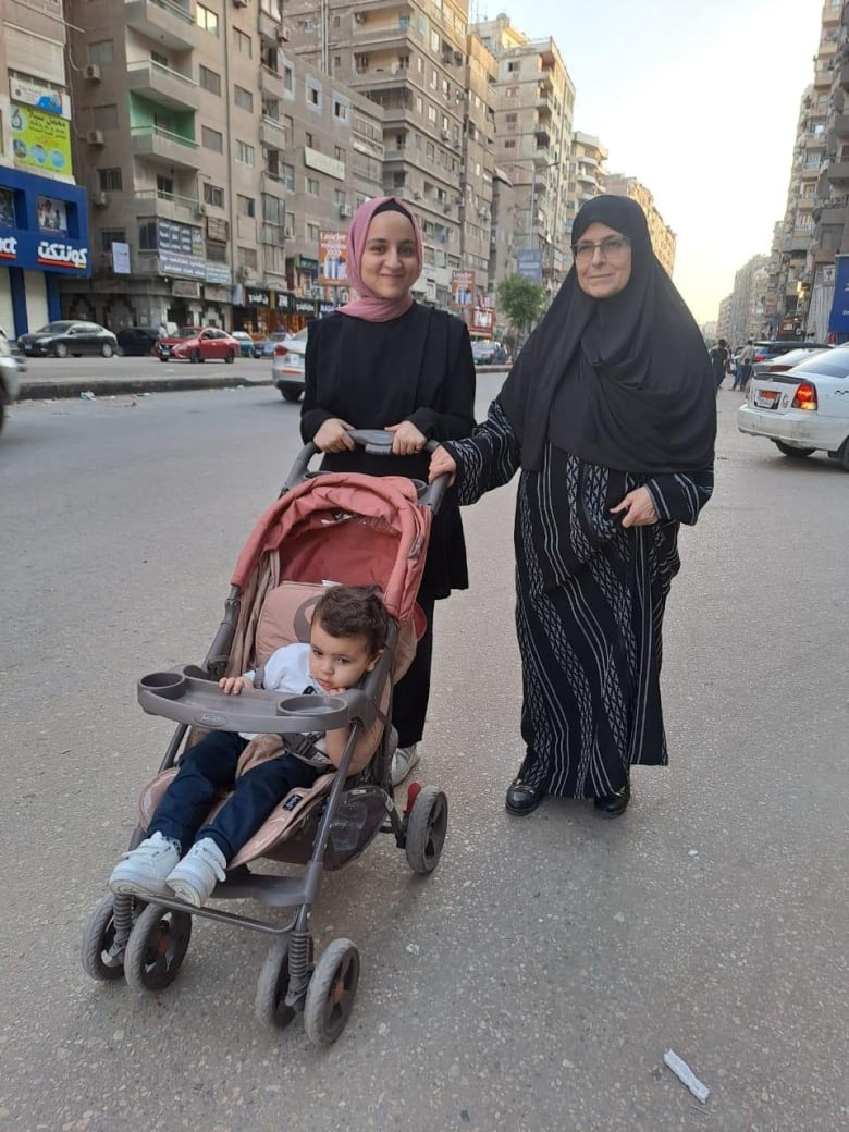 Two smiling women in headscarves push a stroller with a toddler through the streets