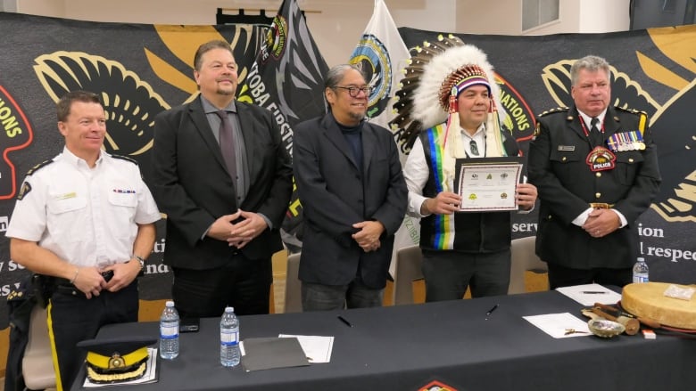 Four people, including police, a First Nations chief and provincial leaders, stand behind a table posing for a photo. 