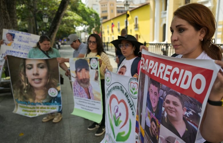 Women gathered in front of a large, yellow building, hold up banners that read MISSING in Spanish and feature photos of their relatives.