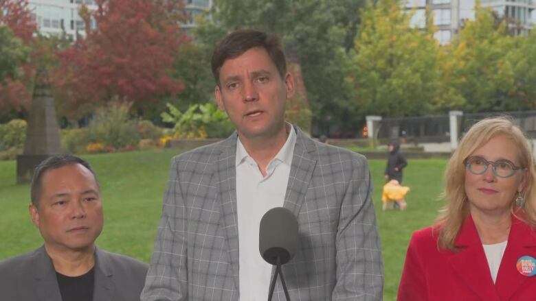 Three people standing in a row outside, in front of green grass. 