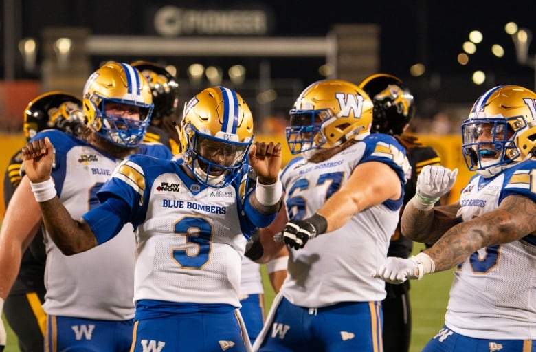 Four football players in white and blue celebrate.