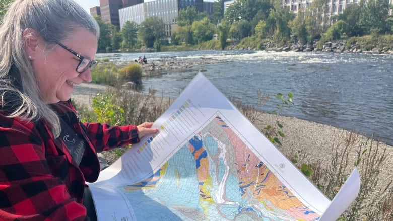 A white woman in a red flannel holds a map of Ottawa.