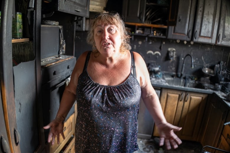 A person gestures while speaking and standing inside a burnt and destroyed kitchen.