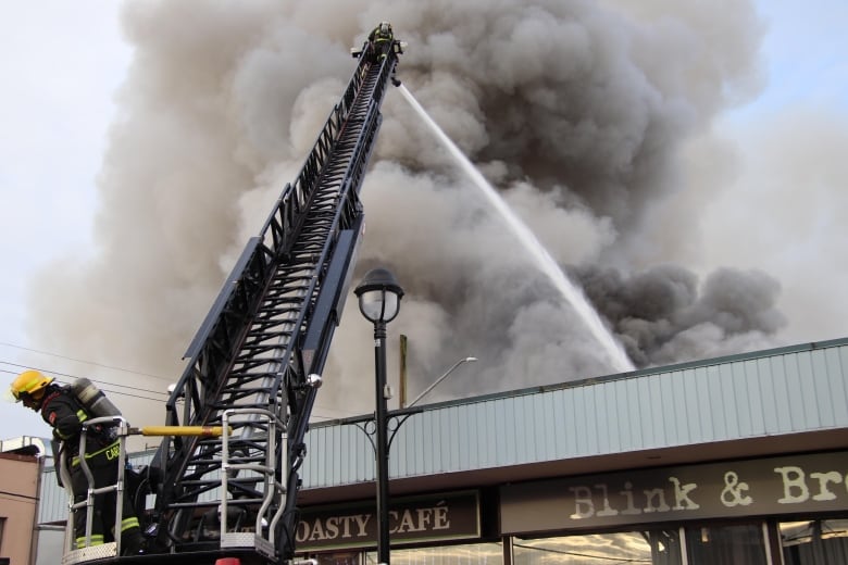 A firefighter atop a ladder sprays a building with water.