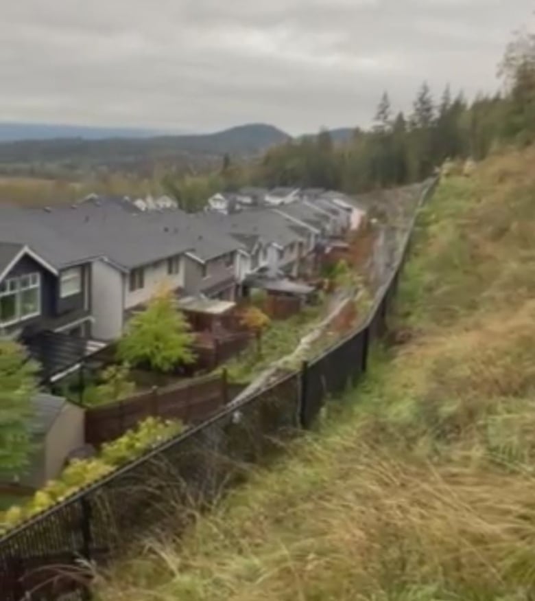 View of a suburban neighbourhood, with grassy hills in the foreground and a line of homes in the background. 