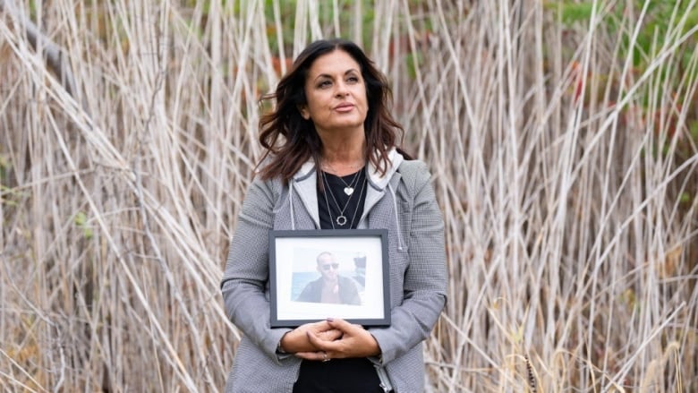 Mother holds framed photo of son who died. 