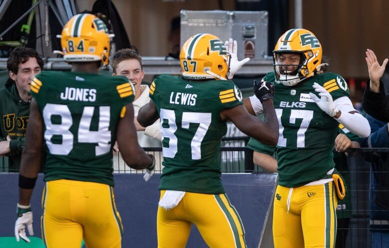 A group of football players in green-and-yellow uniforms are celebrating on the field.