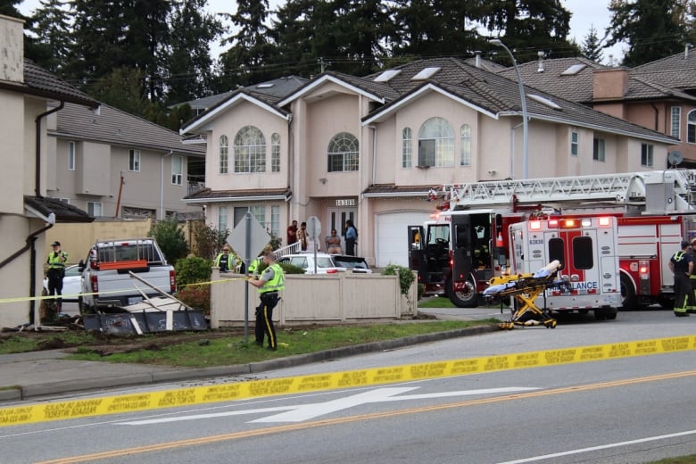 A fire truck and ambulance are in the background, and a white pickup truck lies behind crime tape and a broken fence.