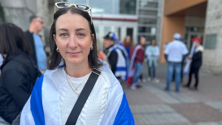 A woman stands in front of Ottawa city hall draped in an Israeli flag