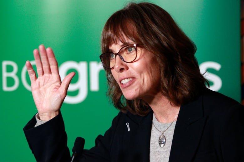 A woman raises her hand in front of a sign reading 'BC Greens'.