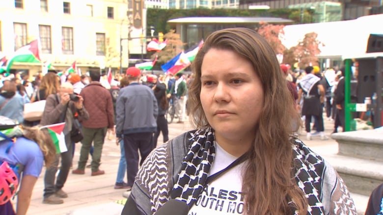 A demonstrator getting interviewed with people waving flags in the background.