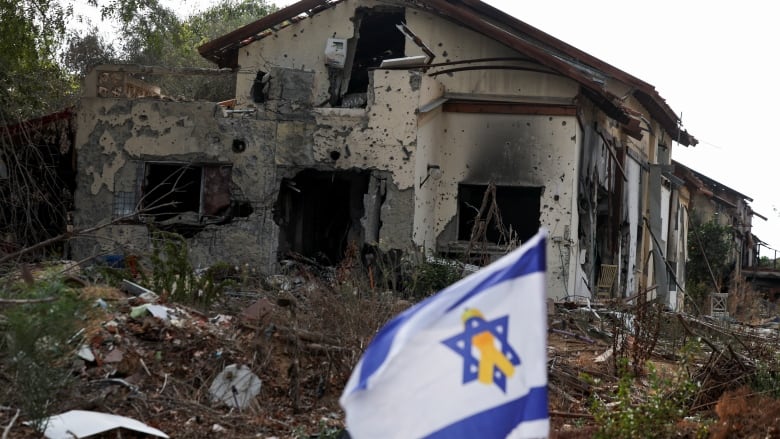 An Israeli flag featuring a yellow ribbon, a symbol of support and solidarity with hostages, flutters near a building damaged during the deadly October 7 attack by Hamas, the day before the first anniversary of the attack, in Kibbutz Beeri in southern Israel, October 6, 2024. 