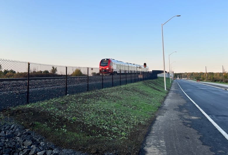 A red public transit train on a rural track on an autumn morning.