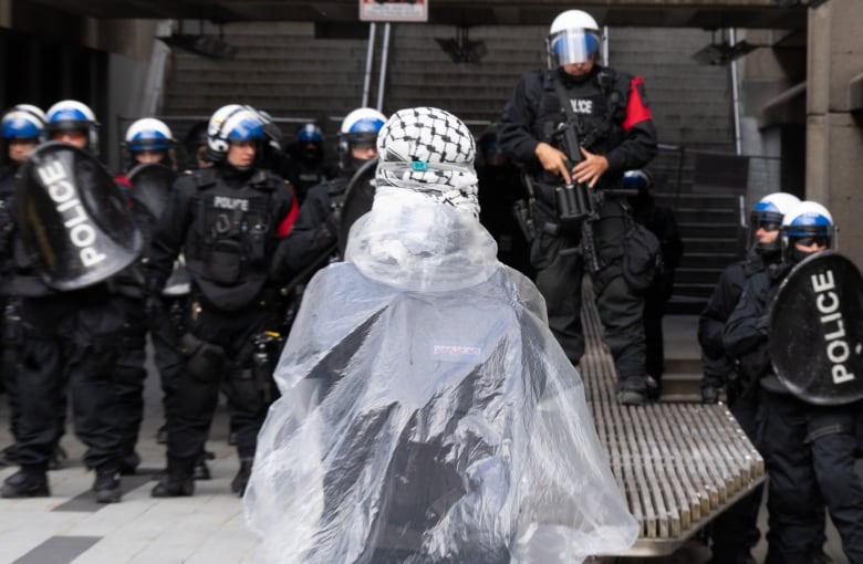 Police are seen in front of a protester wearing a scarf and plastic poncho.