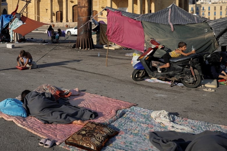 A person lies on a blanket on the street, while a young boy plays on a motorcycle.