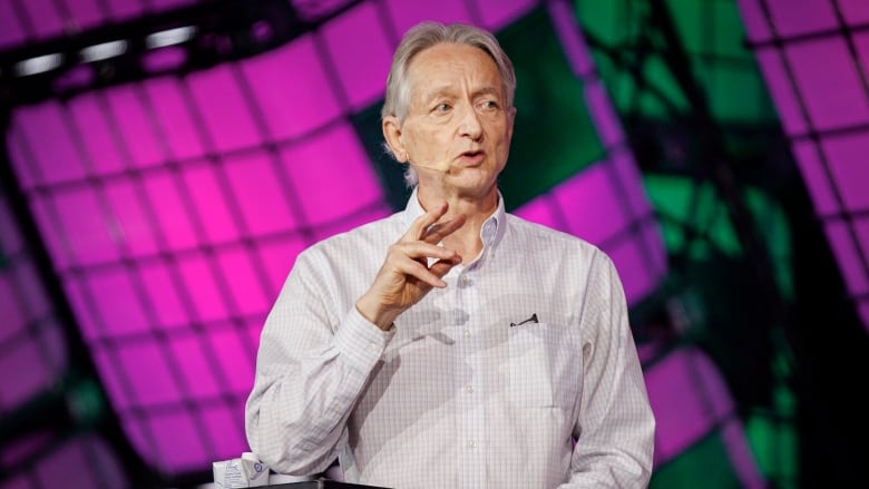 Geoffrey Hinton speaking and gesturing with one hand at a podium on stage.