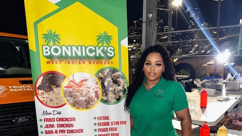 A black woman stands in front of her business. 