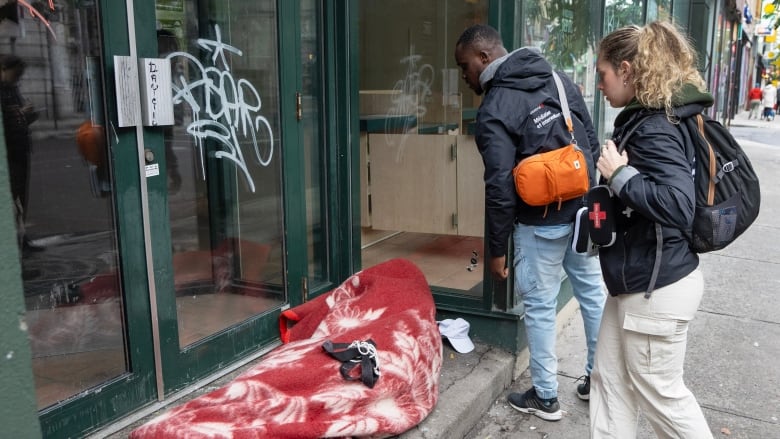 Social workers check on an unhoused person sleeping under a blanket in a shop doorway in Montreal.