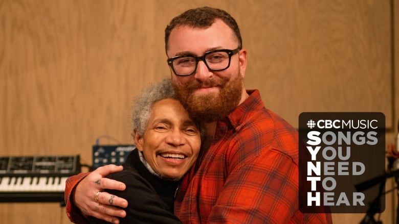 Beverly Glenn Copeland (a Black trans man) and Sam Smith (a white non-binary person) share a warm embrace inside of a recording studio. The CBC Logo and the words 