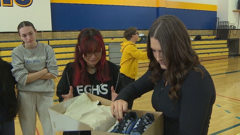 A woman opens a new box of running shoes with a student, who looks excited by the shiny new sneakers. 