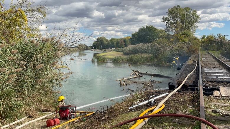 A firefighter sprays water on a charred railway over a river.