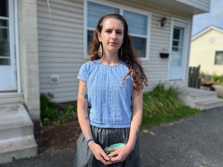 A woman with long hair wearing a blue shirt standing outside a house. 