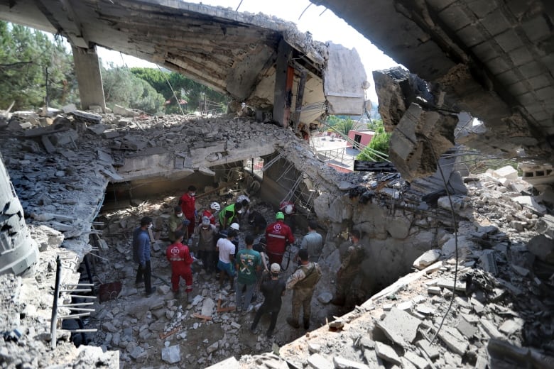 Several people are seen from a distance down at the bottom of a crater where a building has been partially destroyed.