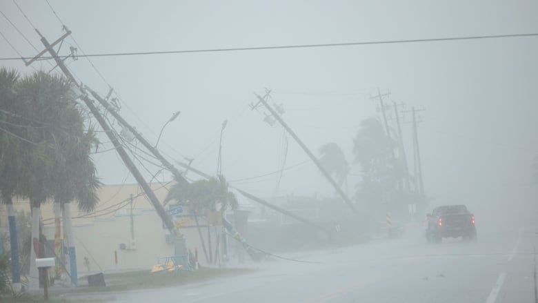 A pickup drives past broken utility poles downed by strong wind gusts