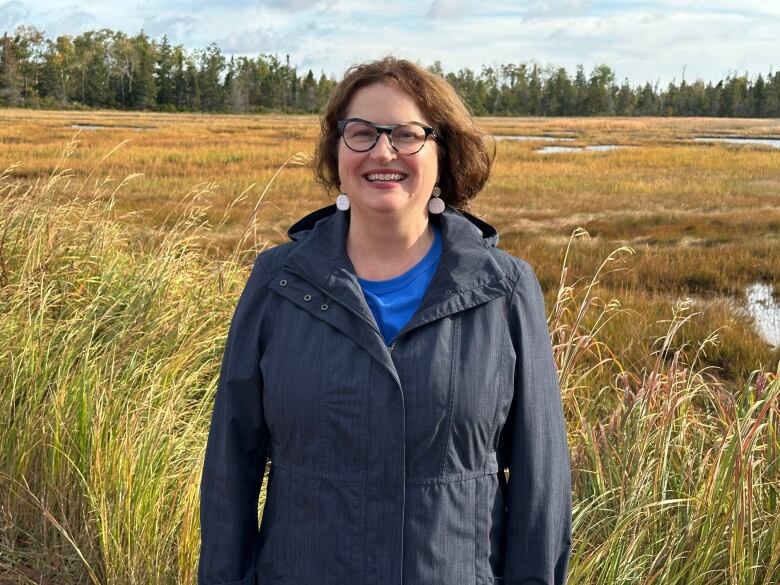 A woman stands near a salt marsh 