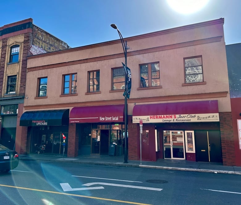 A two-storey stucco building with three separate awnings is seen from across the street. 