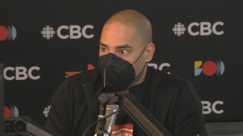 A man wearing a mask speaks at a microphone.