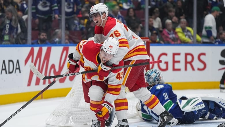 Two hockey players wearing red celebrate as a goalie sits distraught.