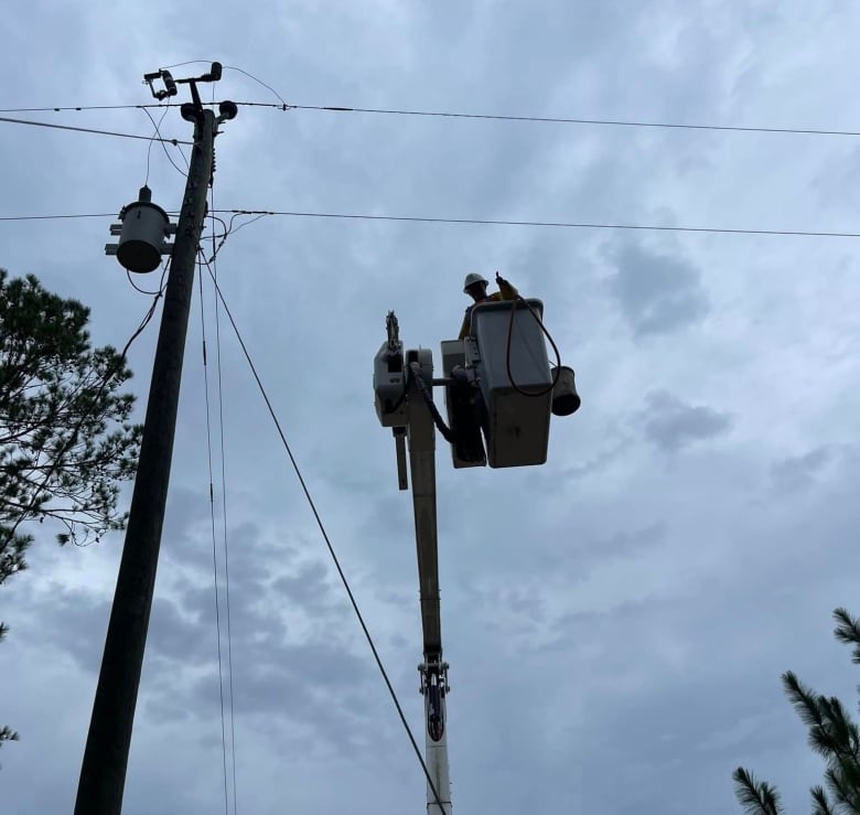 A view looking up at sky next to a pole with someone working on it.