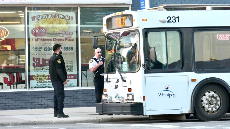 Two police officers stand near the front of a bus. 