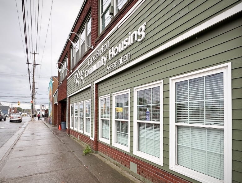 Looking along the sidewalk next to a two-storey red brick building with green siding and white framed windows.