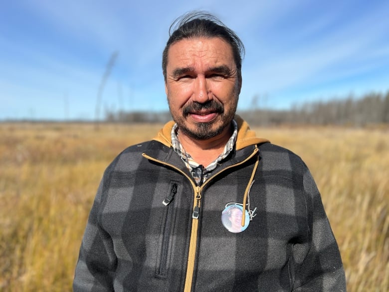 A man with a grey sweater stands on an open field.