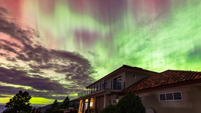 A house is seen in the foreground with the sky alight in ribbons of reds and greens.