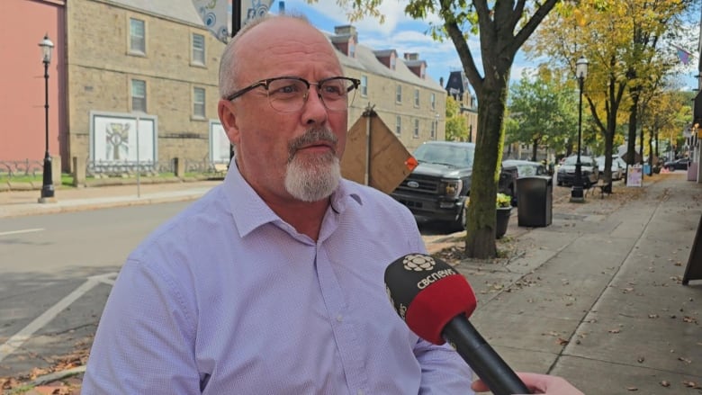 A man in a lilac shirt, speaking into a microphone