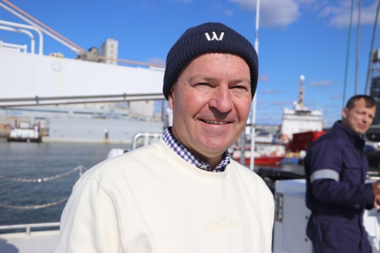 A man smiles at the camera. He is standing on a sailboat. 