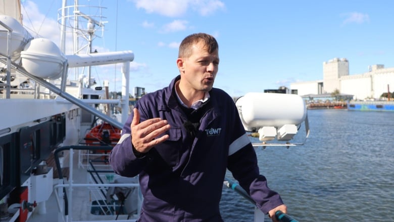 A man waves his hand as he is standing on the deck of a sail boat