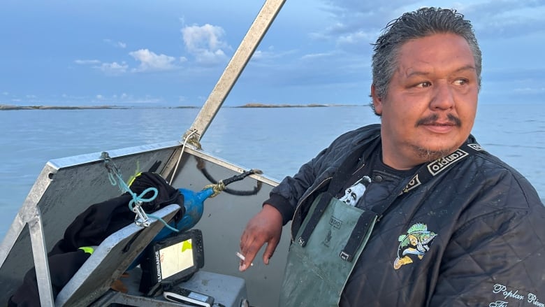 A commercial fisher is pictured behind the wheel of his fishing boat on a large lake.