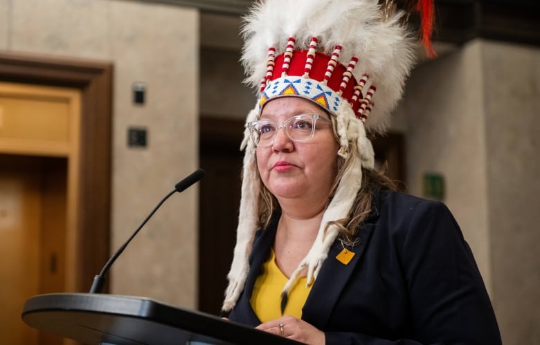 A woman in a headdress speaks at a podium.