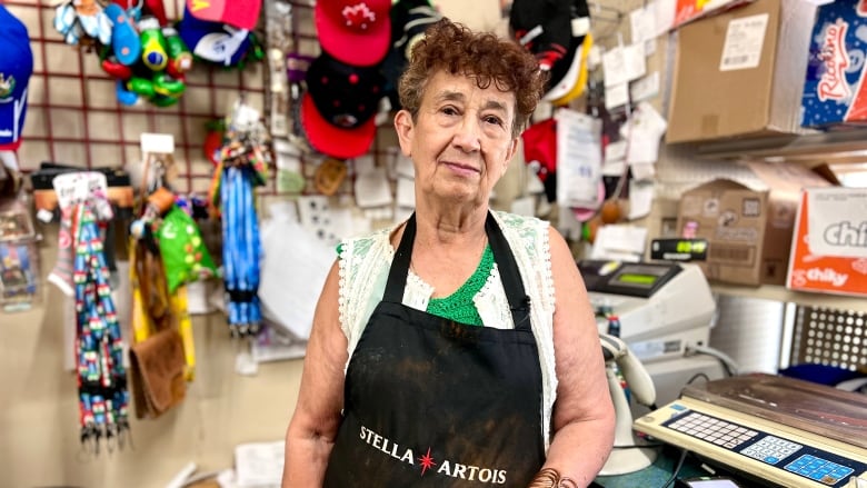 A woman wearing a black apron stands in front of a counter with a cash register on it. 