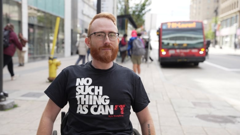 A man in a wheelchair outside of a bus stop and a mall 