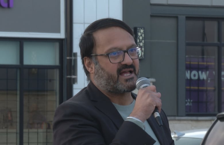 A man wearing a blazer speaks into a microphone.