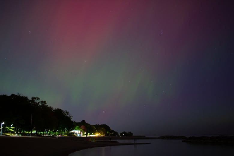 Light tinges of pink and green from the Northern Lights cover the night sky above a beach in Toronto